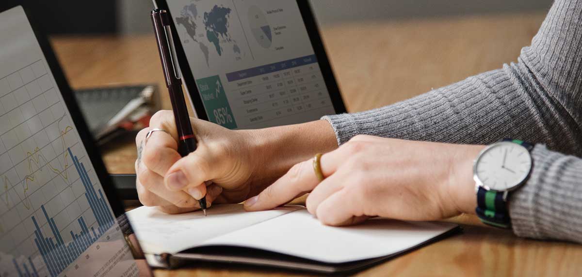 Woman looking at business graphs and writing in a notebook