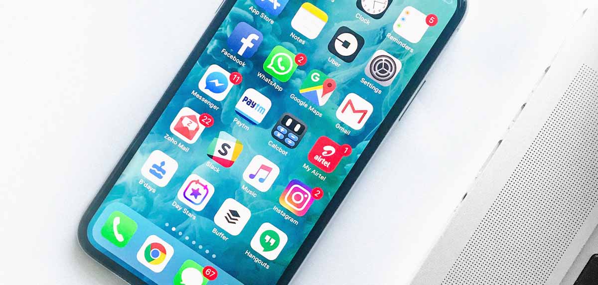 Phone next to Macbook with lots of apps on the home screen